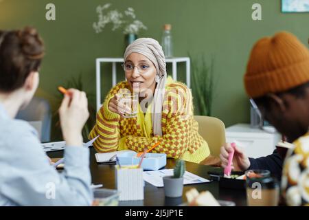 Portrait of creative young woman working with diverse design team at business meeting and enjoying snacks Stock Photo
