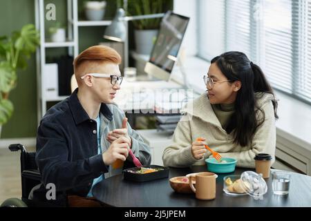Side view portrait of two smiling young people eating lunch at work and enjoying conversation Stock Photo