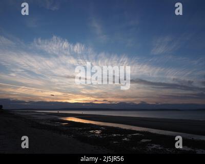 Low tide at Nairn Central Beach, on a summers evening with the sun setting behind a cloud bank & wispy cirrus clouds high in the sky. Stock Photo