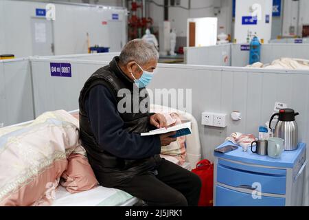Shanghai, China. 23rd Apr, 2022. A senior patient reads a book in a makeshift hospital in Shanghai, east China, April 23, 2022. The makeshift hospital in Lingang is converting around 2,000 beds to treat COVID-19 patients with moderate symptoms and senior patients over 80 years old. Credit: Yang Youzong/Xinhua/Alamy Live News Stock Photo