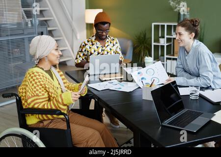 Portrait of diverse creative team working in office with focus on young woman using wheelchair at business meeting Stock Photo