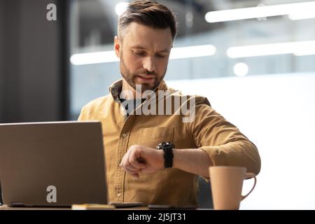 Businessman Using Laptop Checking Time Looking At Watch In Office Stock Photo