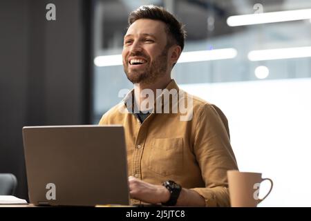 Successful Businessman Using Laptop And Laughing Looking Aside At Workplace Stock Photo
