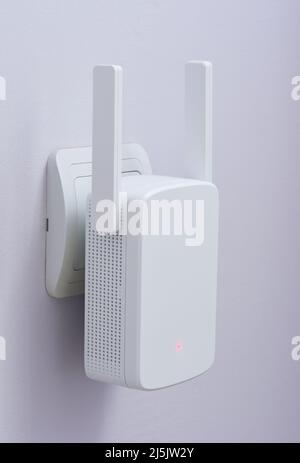 White wi-fi range extender plugged in electrical socket on blue wall Stock Photo