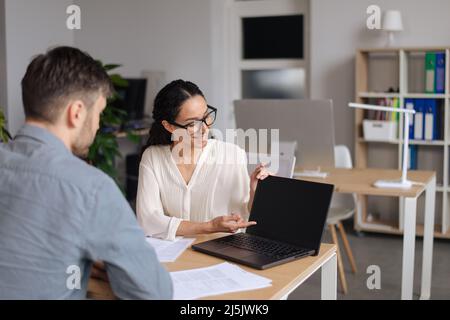 Positive male and female employees discussing business project, using laptop with mockup for website design at office Stock Photo