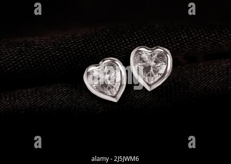 Hearts-shaped silver stud earrings on black fabric background. Stock Photo