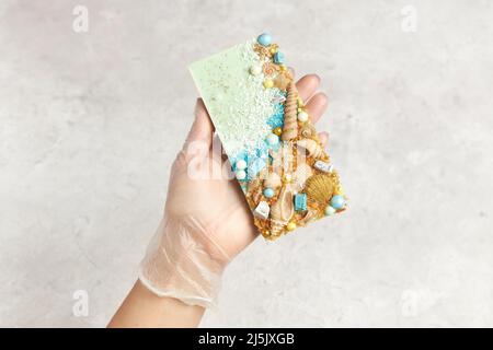 Bar of chocolate decorated with sweets and seashells in the hand of confectioner Stock Photo