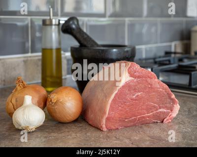 selected focus of a joint of silverside beef  with oil, onions, garic condiments and utensils Stock Photo