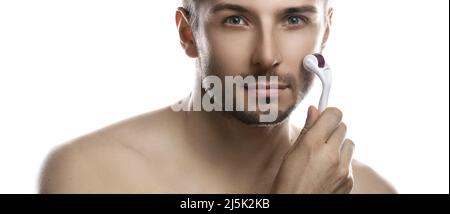 Young handsome man is using derma roller for beard growth on white background Stock Photo