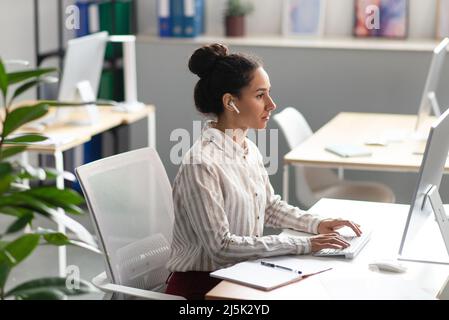 Confident female office worker working on modern computer in office, sitting at workplace, free space Stock Photo