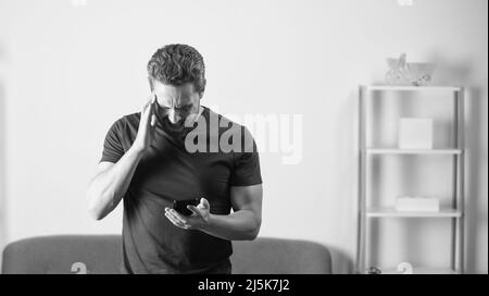 shocked man reading message on phone in office interior, copy space, bad news Stock Photo