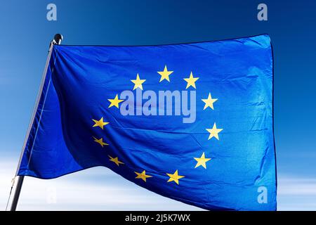 Close-up of an European Union flag waving against a clear blue sky with clouds and copy space. Stock Photo