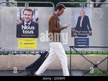 Clichy, France. 24th Apr, 2022. A man walks past electoral posters of Emmanuel Macron and Marine Le Pen in Clichy near Paris, France, April 24, 2022. The 2022 French presidential runoff kicked off at 8 a.m. local time (0600 GMT) on Sunday in Metropolitan France between incumbent President Emmanuel Macron and candidate Marine Le Pen. Credit: Gao Jing/Xinhua/Alamy Live News Stock Photo