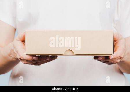 Woman hands holding brown ecological package box made of natural corrugated cardboard. Mockup mailing parcel box on blue background. Packaging Stock Photo