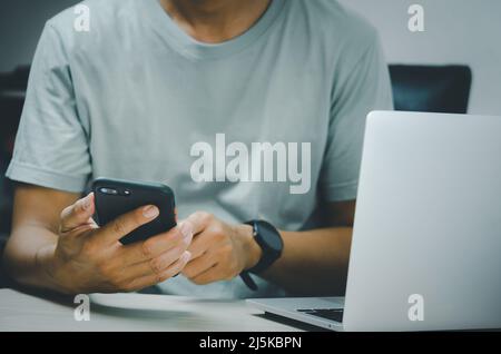 man hand holding smartphone and computer laptop to working technology searching internet, sending sms, using text messenger or online banking. Stock Photo