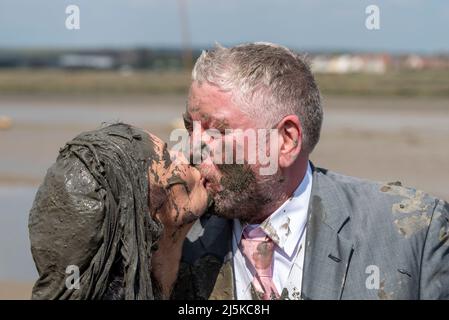 Maldon Promenade Park, Maldon, Essex, UK. 24th Apr, 2022. Large numbers of runners tackled the gruelling course which took them across the River Blackwater and back at low tide, through the clinging slippery mud. The Maldon Mud Race competitors run for charity, with many in fancy dress and all get covered in slimy mud during the race, especially those behind once the mud becomes churned up. Recently married couple in their wedding attire. Dominique and Matt Sellors kissing after completing the course Stock Photo