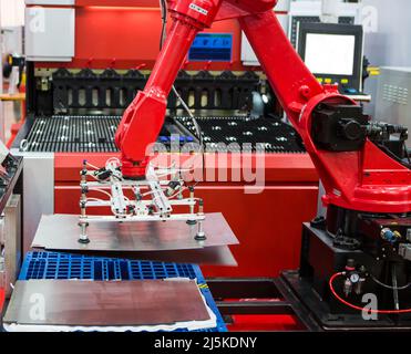 Robot arm loading metal sheet to laser cutting machine in production line. Industrial metalworking machinery. Stock Photo