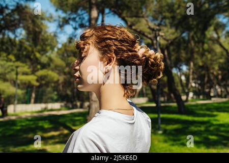 Calm beautiful redhead young woman with curly hair enjoying fresh air outdoor, relaxing with eyes closed, feeling alive, breathing, dreaming. Stock Photo