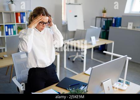Mature tired business woman with headache in office. Overworked female employee holding her head Stock Photo