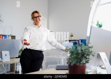 Friendly female office worker in glasses and formal wear showing welcome gesture Stock Photo
