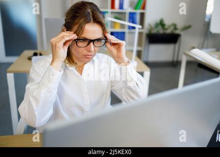 Mature female office worker is concentrated and attentively looking at the computer screen Stock Photo