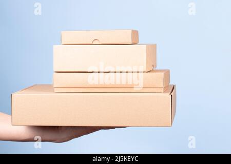 Stack of cardboard boxes in female hands. Blank brown parcel boxes on light blue background. Packaging, shopping, free shipping, delivery concept Stock Photo