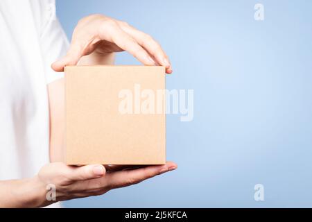 Female hands holding brown rectangular cardboard box on light blue background. Mockup parcel box. Packaging, shopping, delivery concept Stock Photo