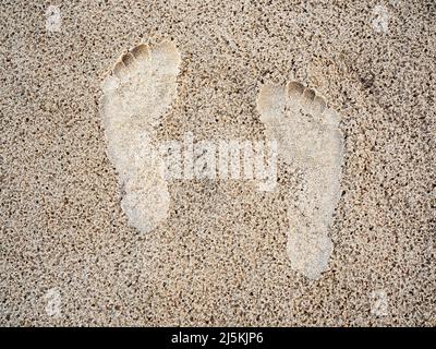 Close-up footprint in the sand beach background. Human foot step track on the wet sand texture, top view. Vacation, holiday, and summer concept. Stock Photo