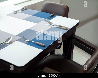 Fork, spoons and knives with empty space on the blue placemat on white table for the guests at the breakfast room in hotel. Stock Photo