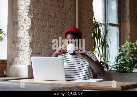 Black man talking on mobile phone, drinking coffee, remotely online work on laptop in cafe Stock Photo