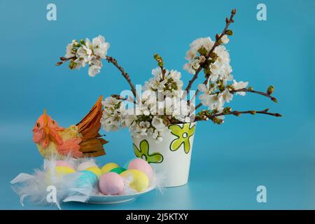Toy handmade hen  with a nest of colored eggs and branches of a blossoming apple tree in a vase on a blue background Stock Photo