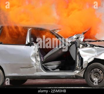 very thick orange smoke coming out of the crashed car completely destroyed after the traffic accident on the highway Stock Photo
