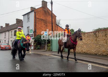 Female riders wearing a Christmas hat riding horses dressed up in tinsel along a street in the centre of Newport Pagnell, Buckinghamshire, England, UK Stock Photo