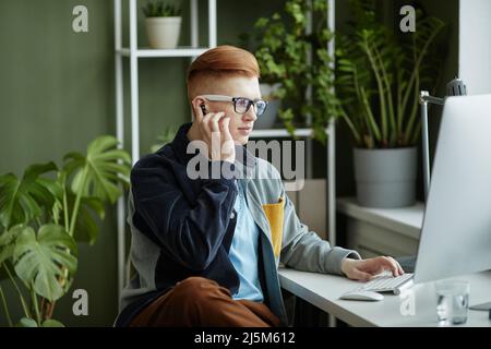 Portrait of trendy young businessman using computer while working at desk in green office Stock Photo