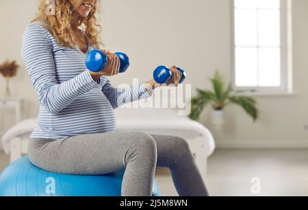 Pregnant woman exercising with fit ball and dumbbells during pregnancy workout at home Stock Photo