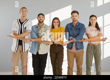 Team of happy, cheerful young people standing together, holding hands and smiling Stock Photo