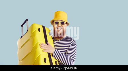 Funny chubby traveler in swimsuit, hat and sunglasses holding yellow suitcase and smiling Stock Photo