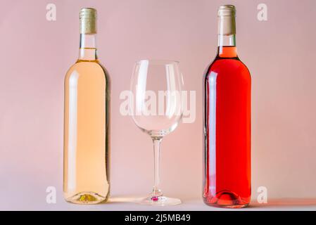 Two bottles of wine, one rosé and the other white, with an empty glass between the two. Stock Photo