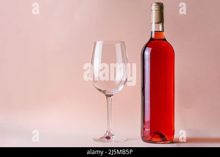 Bottle of rose wine next to a glass on a salmon colored background. Stock Photo
