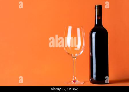 Bottle of red wine next to an empty glass on an orange background. Stock Photo