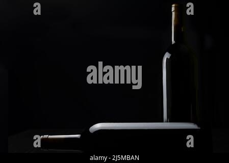 Two bottles of red wine, one lying on the bottom and the other standing on the side, with little light, revealing only the relief of the glass, on a b Stock Photo
