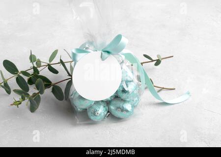 Small gift with chocolate easter eggs in a plastic bag with a bow of mint color ribbon and a round white gift tag mockup Stock Photo