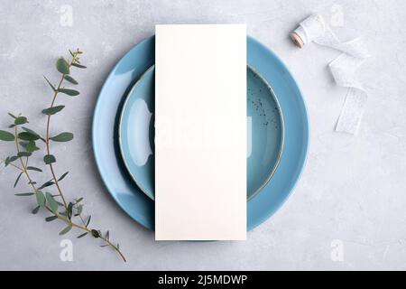 Menu card mockup on blue plate with festive wedding or birthday table setting with eucalyptus branch on grey background Stock Photo