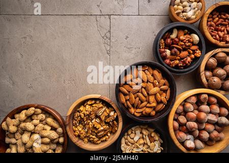 Assortment of nuts in bowls on stone background top view with copy space. Healthy snack food. Stock Photo