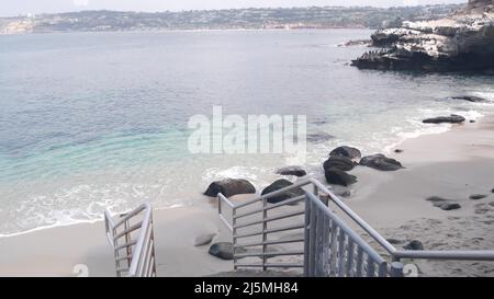 Beach access, stairs to crystal blue azure transparent calm ocean, La Jolla cove, California coast, USA. Turquoise clear sea waves. Water surface and sand, tropical paradise lagoon, summer vacations. Stock Photo