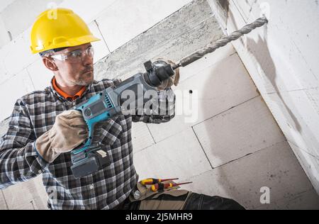 Caucasian Construction Worker in His 40s with Powerful Hammer Drill. Drilling Necessary a Hole Inside Concrete Bricks Wall. Stock Photo