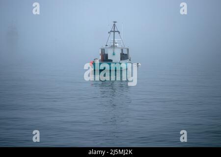 An anchored fishing boat visible through fog in Chatham Harbor, Chatham, Massachusetts, on Cape Cod Stock Photo