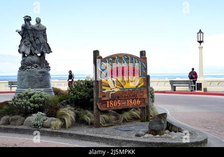 A sign on the waterfront for the coastal holiday town of Seaside, Oregon, USA with a statue of explorers Lewis and Clark at left. Stock Photo