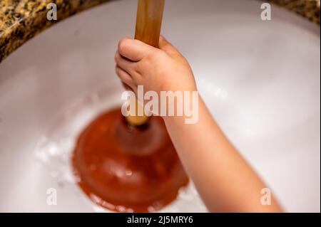Using a plunger on a bathroom sink plugged with Hair and scum in a pool of stagnant standing water. Stock Photo