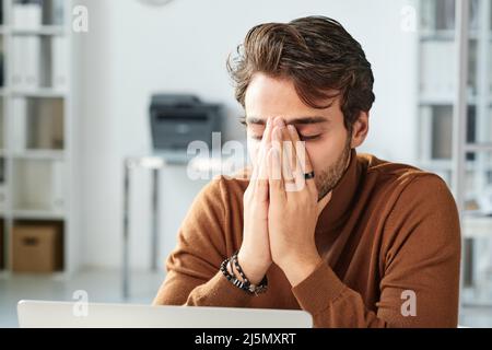 Confused young middle eastern manager with stubble being stressed out and covering face with hands in office Stock Photo